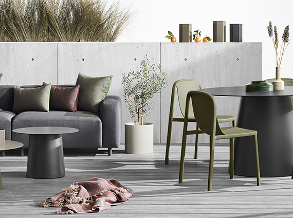 Blu Dot grey sofa with pillows, near a black circular table next to forest green chairs