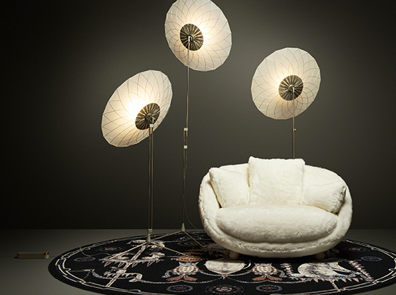Filigree floor lamps, attached to white shades and intricate metalwork, next to a white chenille love sofa with pillows in a dark toned room