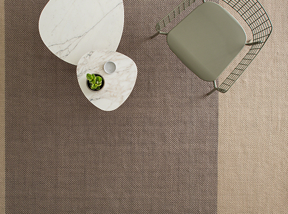 Diagonal outdoor rug in a sand color with light brown center line and chair with side tables