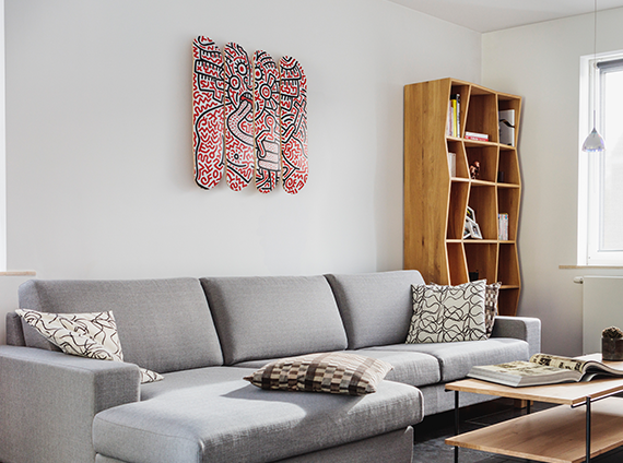 Vibrant red skateboard deck art by Keith Haring, mounted above a grey couch in a living room