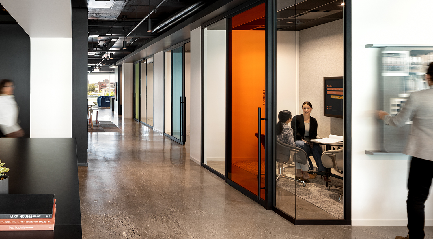 View of hallway, glass wall into variety of rooms, each with colored glass, orange, blue and green