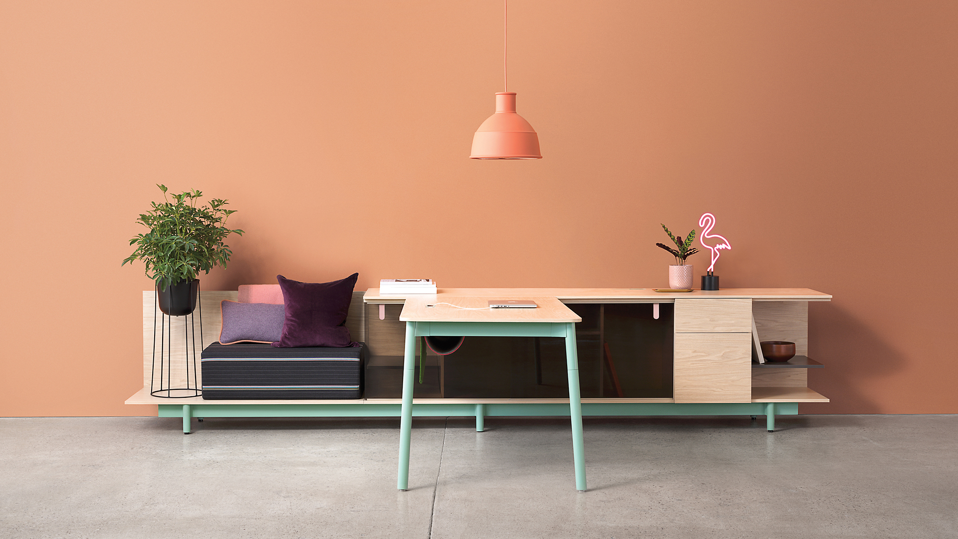 A maple and mint green desk with bench and storage in front of a peach wall