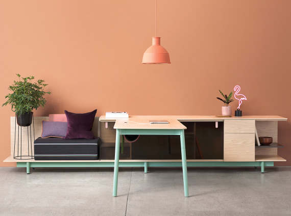 A maple and mint green desk with bench and storage in front of a peach wall